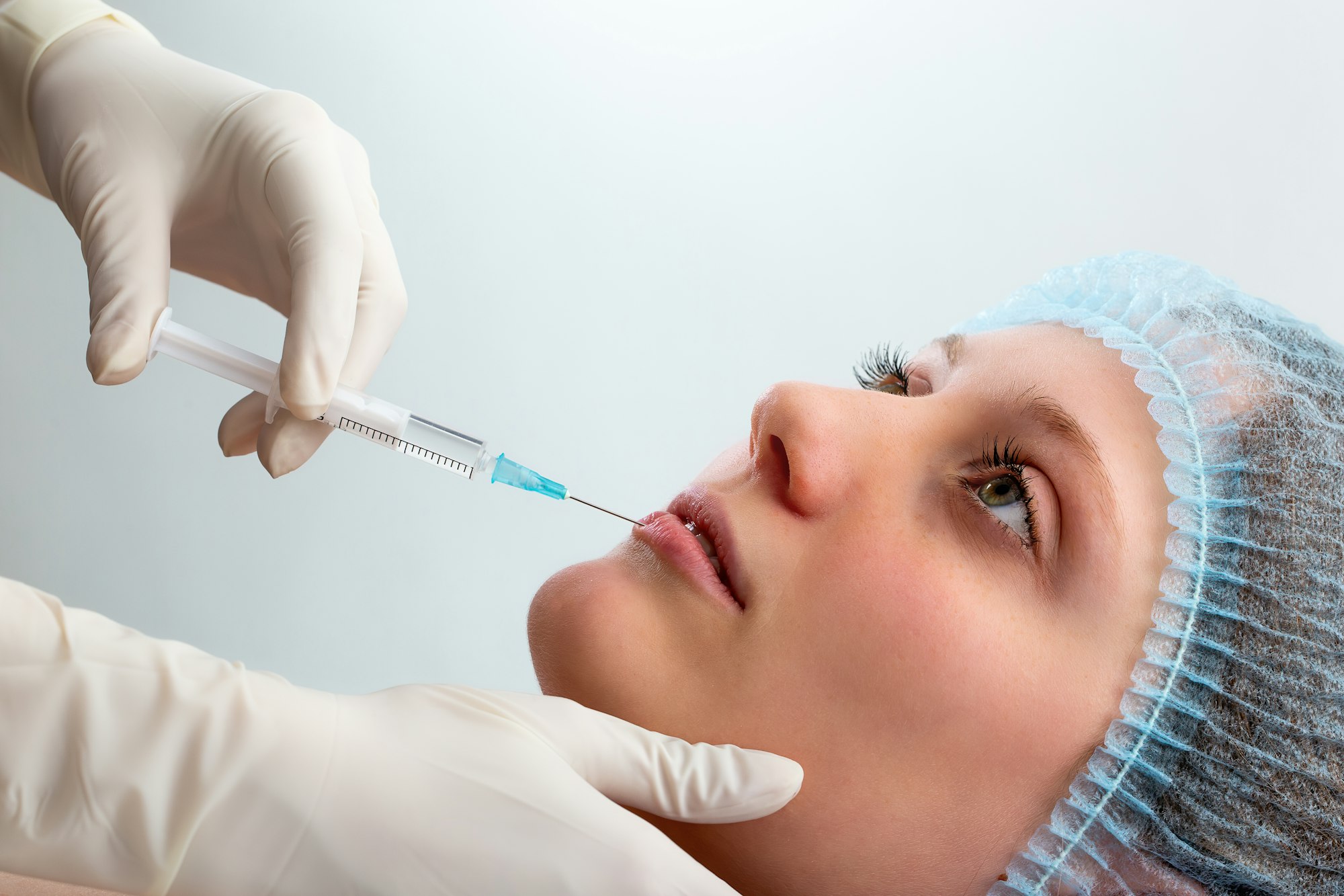 Cosmetic surgeon injecting botox to lower lip of a young woman